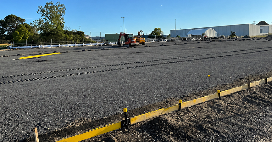 An expansive equestrian riding arena under construction featuring a compacted gravel base. The site shows the use of string lines and stakes to mark out dressage arena dimensions, such as 20 meters by 60 meters, while preparing the drainage system for a high quality finish.