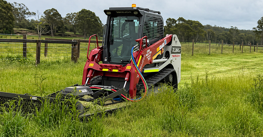 Specialized machinery clearing long grass on a rural property to begin equine arena construction. Equestrian riding arena preparation often starts with land clearing and site assessment before finalizing the arena size and seeking necessary Council Permits or DA Approval.